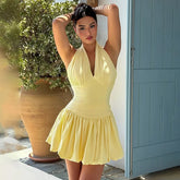 Woman in a yellow dress standing outdoors near a blue door and potted plant.